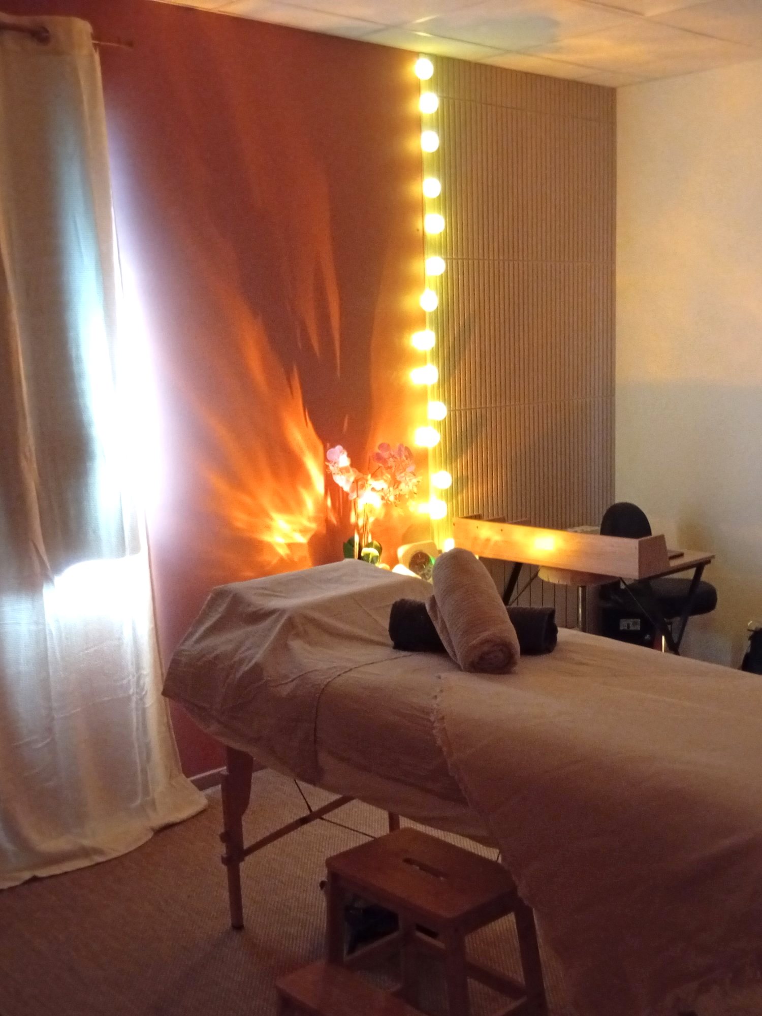 Cabine de Grand Fougeray en lumière tamisée, table de massage et guirlande lumineuse